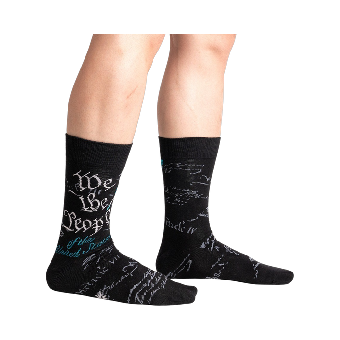 Lifestyle shot showing The Constitution socks on a person's legs. The socks are black with teal and gray text.
