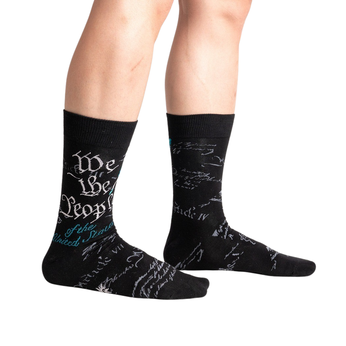 A pair of black socks with the US constitution written in white and blue on the back of the socks.