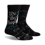 Pair of black crew socks featuring the text of the US Constitution preamble in teal and gray. A quill and ink design is subtly present.