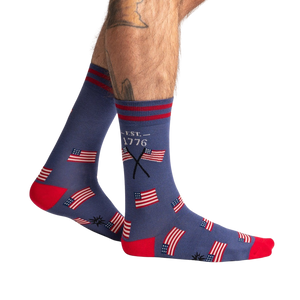 A pair of blue socks with a red toe and red and white striped cuff. The socks have a pattern of American flags on them.