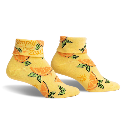 front view of two pairs of yellow socks with orange slices and green leaves on them.  the top of the socks says "simply the zest".