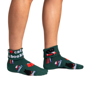 front view of a person wearing green ankle socks with a black cat, books and a red heart on them. one sock says, 