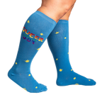 Lifestyle shot: Person wearing blue knee-high socks with 'Queer Joy' and stars. Shows the fit and style.