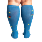 Rear view of model wearing blue knee-high socks featuring 'Queer Joy' in rainbow and yellow stars.