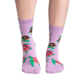 Lifestyle shot of model wearing a pair of lavender crew socks with turtles and donuts.