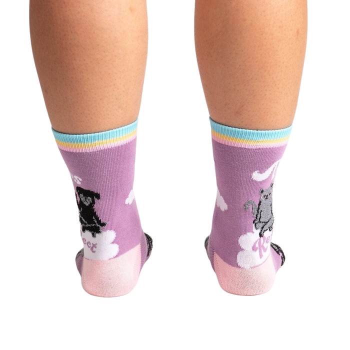 A pair of purple socks with a black dog and a gray cat on them. The socks have a rainbow and clouds at the top and a pink toe and heel.