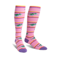 Knee-high socks in pink with purple cuffs.  Design features green T-Rexes on roller skates skating across pink and yellow stripes.