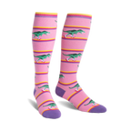 Knee-high socks in pink with purple cuffs.  Design features green T-Rexes on roller skates skating across pink and yellow stripes.