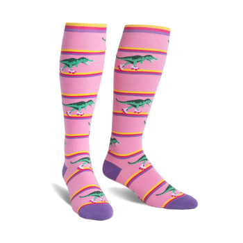Pair of pink knee-high socks with a pattern of green roller-skating T-Rex dinosaurs and horizontal yellow, pink, and purple stripes.