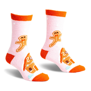 front view of a pair of pink fuzzy socks with orange trim. the socks feature gingerbread men and gingerbread houses.