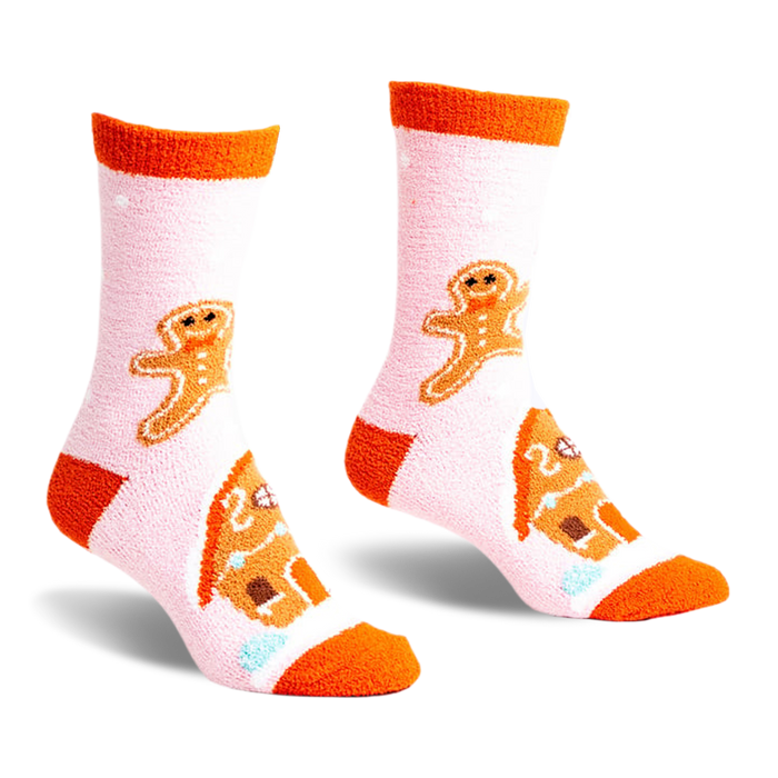 front view of a pair of pink fuzzy socks with orange trim. the socks feature gingerbread men and gingerbread houses.