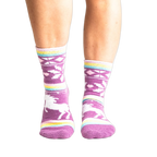 Lifestyle shot: Woman's legs wearing purple unicorn slipper socks.