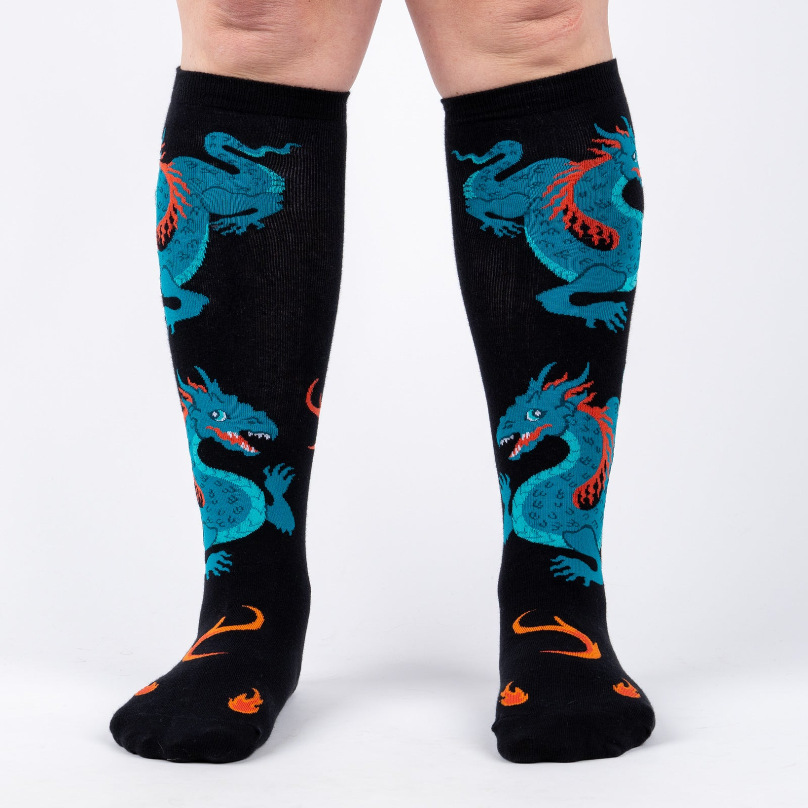 Front view of model wearing a pair of black knee-high socks with teal dragons and orange flames.