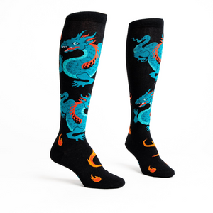 Flat lay studio shot of a pair of black knee-high socks with teal dragons and orange flames.