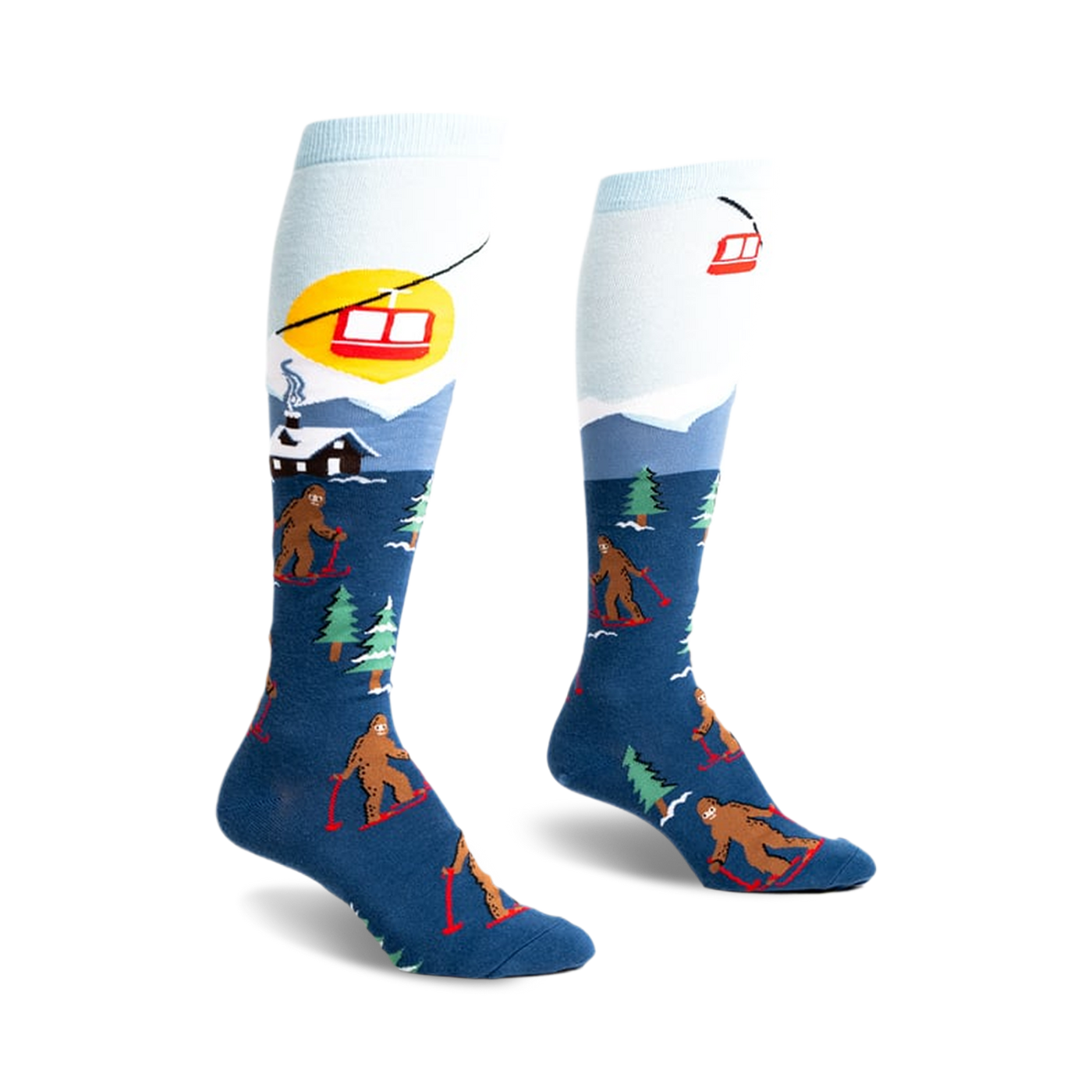 Pair of blue and light blue knee-high socks. Design features Bigfoot skiing, a snowy mountain scene, and a ski lift.