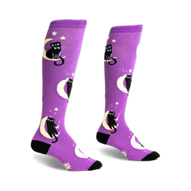 a pair of purple knee-high socks with black cats sitting on the moon. the socks have a white crescent moon with a black cat sitting on top of it. the cat has a blue bow tie and there are stars on the socks as well. the socks are shown from the side.