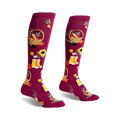 Pair of burgundy knee-high socks with autumn harvest design: pumpkins, sunflowers, baskets, and yellow boots.