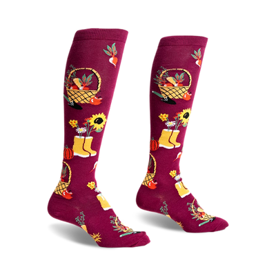 pair of knee-high socks with a garden theme. the socks are burgundy with yellow, green, and orange accents.  the socks feature a basket of fruit, flowers in a pot, and a pair of yellow rain boots. the image shows the socks from the side.  the socks are on a white background.