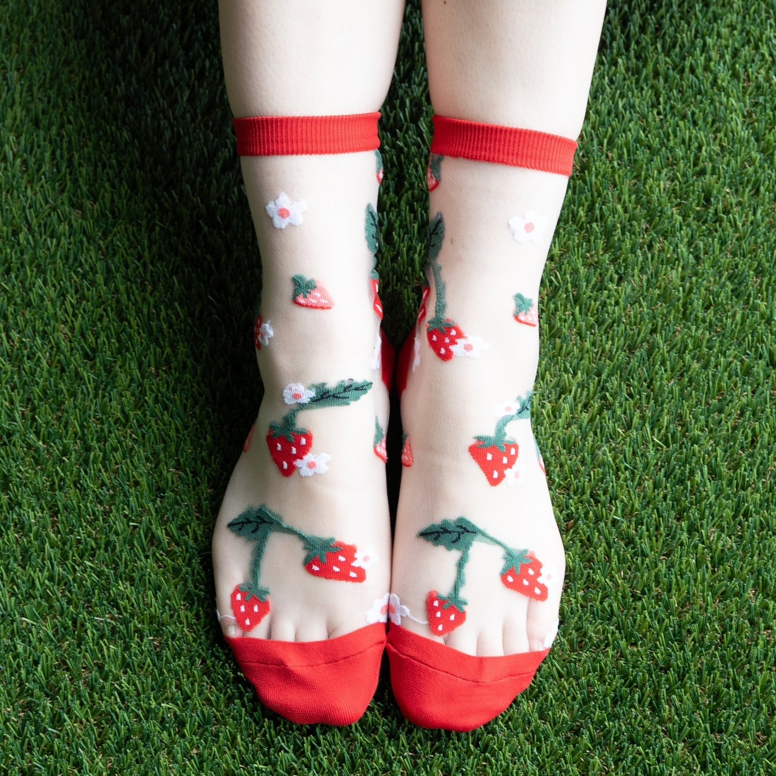 [lf] Legs in sheer strawberry and flower socks stand on green artificial grass.