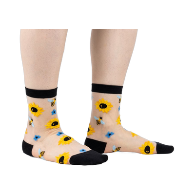 Sheer ankle socks with sunflowers and bees.  Beige background, black cuffs, yellow sunflowers, and blue bees.