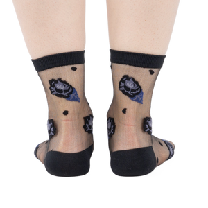 Rear view of legs wearing sheer black ankle socks with dark blue and black rose patterns and black dots on a white background.