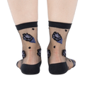 Rear view of legs wearing sheer black ankle socks with dark blue and black rose patterns and black dots on a white background.