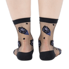 Rear view of legs wearing sheer black ankle socks with dark blue and black rose patterns and black dots on a white background.
