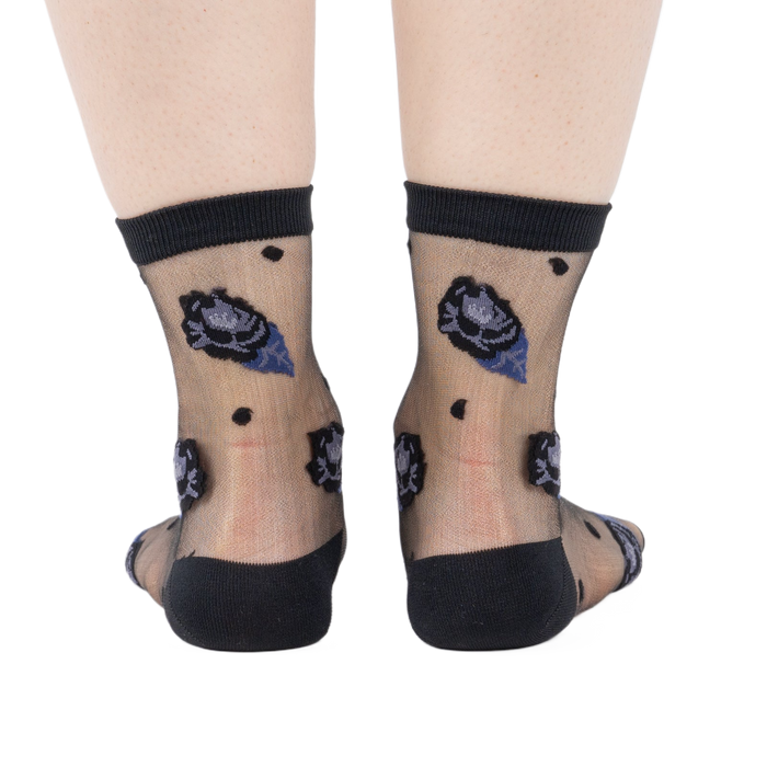 Rear view of legs wearing sheer black ankle socks with dark blue and black rose patterns and black dots on a white background.