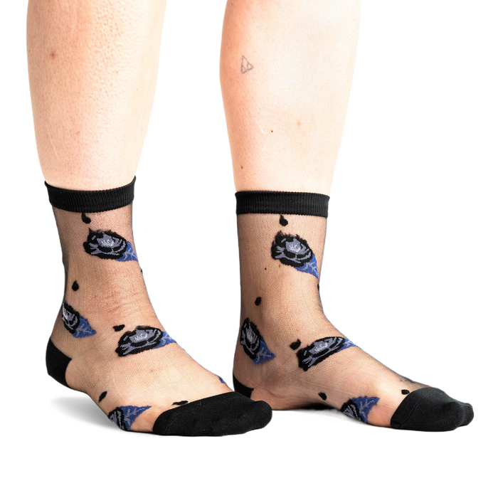 Front view of legs wearing sheer black ankle socks with dark blue and black rose patterns and small black dots on a white background.