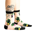 A pair of sheer ankle socks with a black band at the top, featuring a whimsical repeating pattern of black cats in yellow and green plant pots.