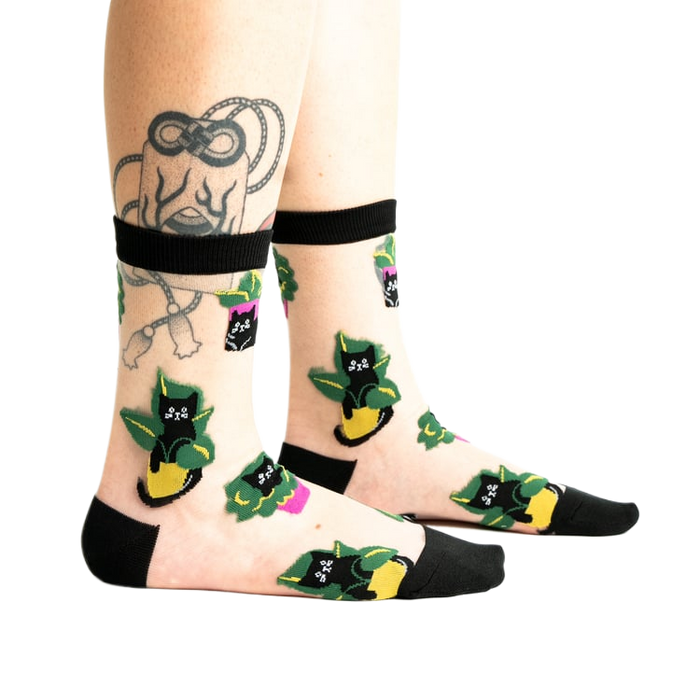 front view of a woman's feet wearing pink high heeled shoes.  she is wearing sheer socks with a black cat and green plant design.