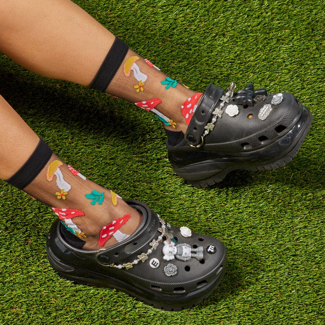 [lf] Legs crossed on grass, wearing sheer black socks with colorful mushroom and leaf patterns.