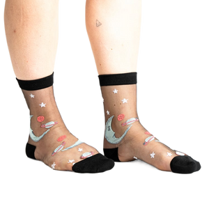 front view of a woman's feet wearing black sheer socks with a white star and a moon and planet pattern. the socks are worn with bright blue platform sandals.