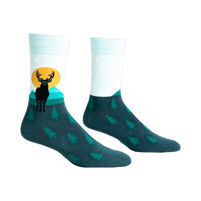 Pair of teal and mint crew socks featuring a black deer silhouette against a yellow sun and teal mountains.  Small pine trees cover the bottom.