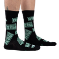 Lifestyle shot of model's legs wearing the black crew socks with a green $100 bill pattern.