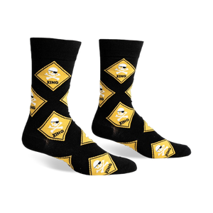 Black crew socks with a repeating pattern of yellow diamond-shaped warning signs featuring skulls wearing sunglasses and crossbones.
