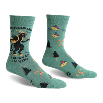 front view of a pair of green socks with a christmas theme. the socks have a black and white image of a krampus on one sock and a repeated pattern of christmas trees, candy canes, and bells on the other sock. the text "krampus believes in you" is written on the sock with the krampus image.