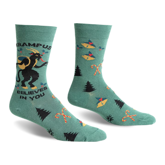 front view of a pair of green socks with a christmas theme. the socks have a black and white image of a krampus on one sock and a repeated pattern of christmas trees, candy canes, and bells on the other sock. the text 