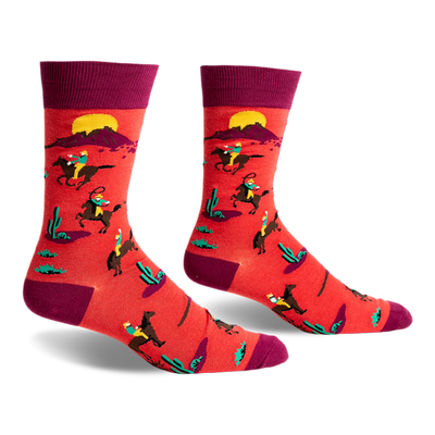 front view of a pair of red socks with a pattern of people riding horses in a desert landscape. the socks are maroon at the top.