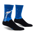 Pair of blue and black crew socks. Design features a giraffe looking up at a UFO against a night sky with stars and a silhouetted landscape.