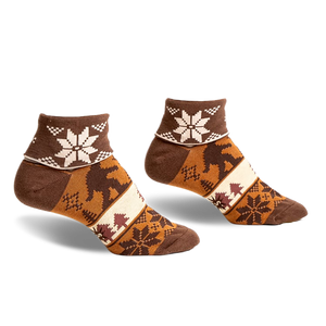 pair of brown ankle socks with a tan, white and brown snowflake pattern. the socks have a brown silhouette of a bigfoot walking through a forest scene. the socks are photographed from the side.