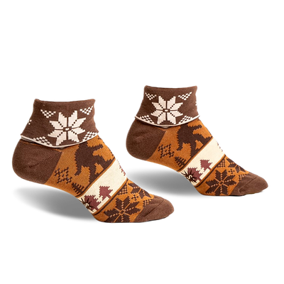 pair of brown ankle socks with a tan, white and brown snowflake pattern. the socks have a brown silhouette of a bigfoot walking through a forest scene. the socks are photographed from the side.