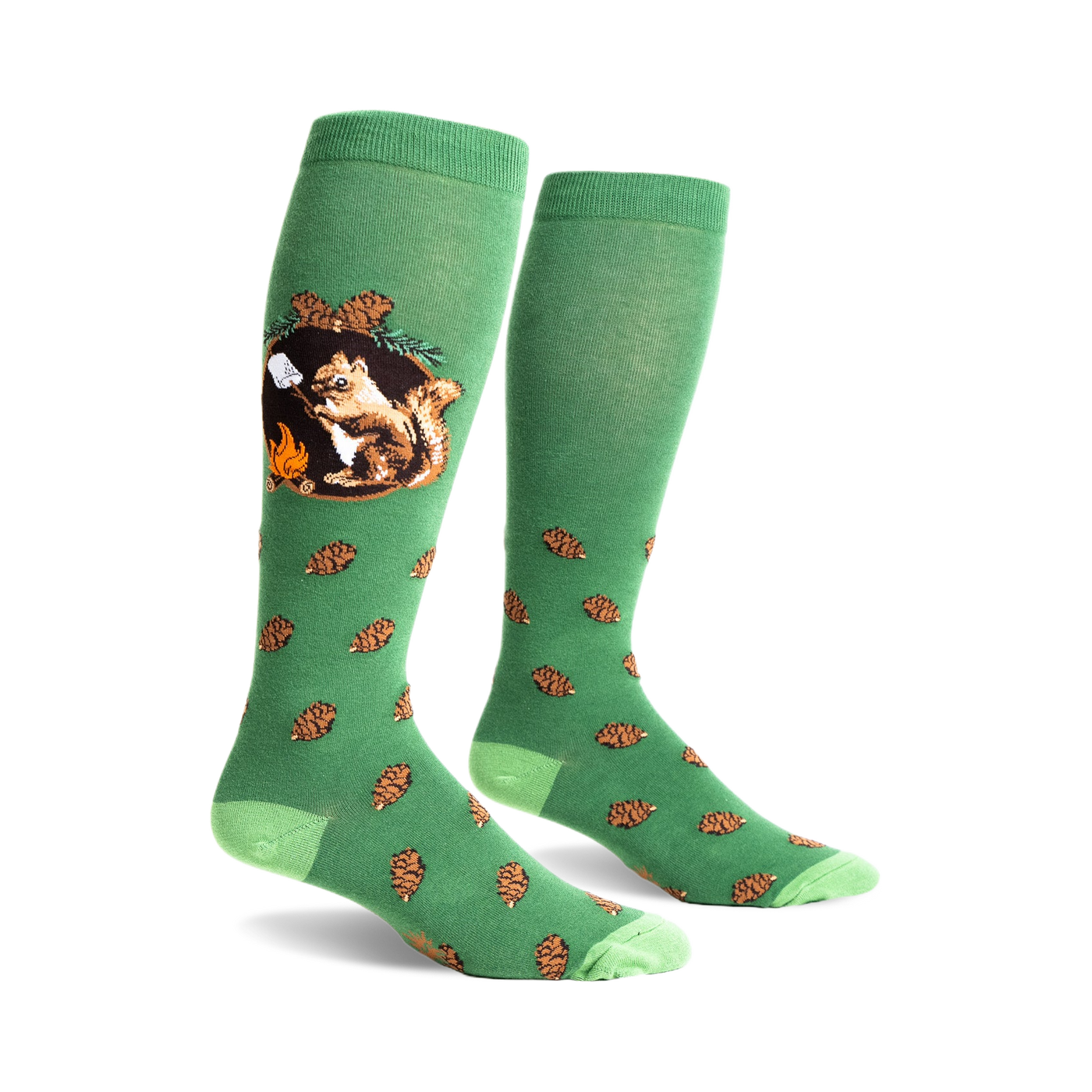A pair of green knee-high socks with a whimsical design. One sock shows a squirrel roasting a marshmallow by a campfire; the other has scattered pine cones.