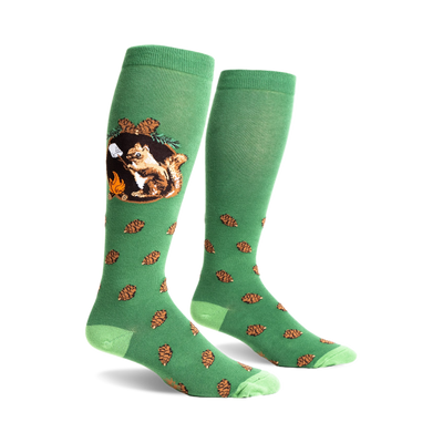 Pair of green crew socks with a squirrel roasting a marshmallow over a campfire, surrounded by pinecones. Light green toe/heel.