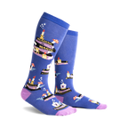 Pair of blue knee-high socks with a whimsical design featuring stacks of books, candles, and mushrooms. Purple accents at the cuff.