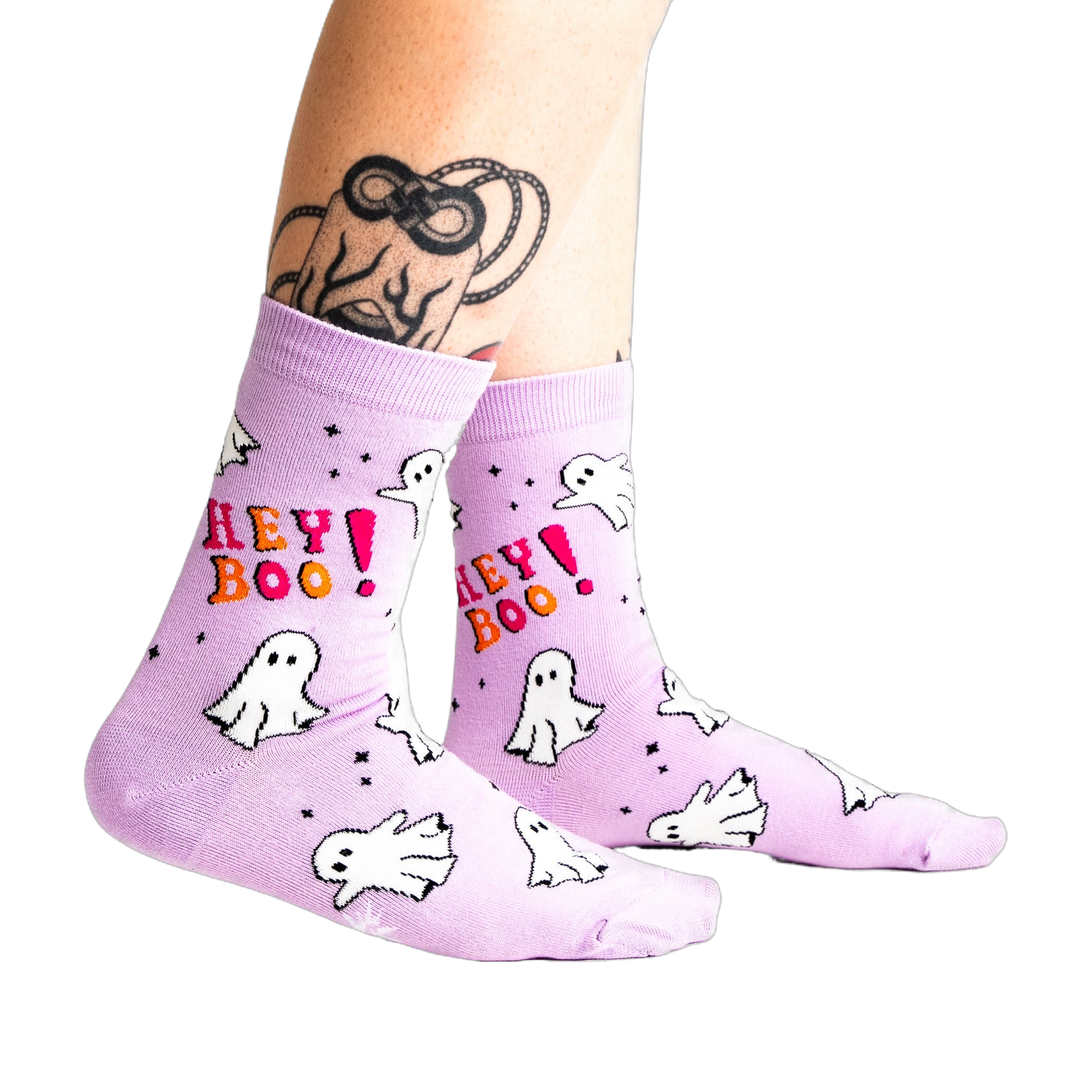 A person's tattooed legs wearing the light lavender "Hey Boo!" ghost crew socks. A "Glows in the Dark" star graphic is visible.