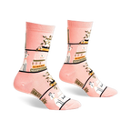 Pair of pink crew socks with a whimsical design of books, plants, and white dogs on a blush pink background.