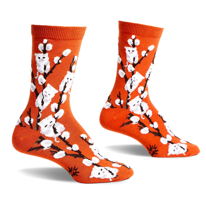 Pair of orange crew socks with a whimsical design featuring white kittens playfully perched on willow branches.