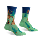 Crew socks in green and navy blue featuring a Bigfoot camping scene with trees, a campfire, and a Bigfoot playing a banjo under a starry night sky.