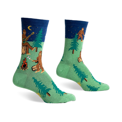 Crew socks in green and navy blue featuring a Bigfoot camping scene with trees, a campfire, and a Bigfoot playing a banjo under a starry night sky.